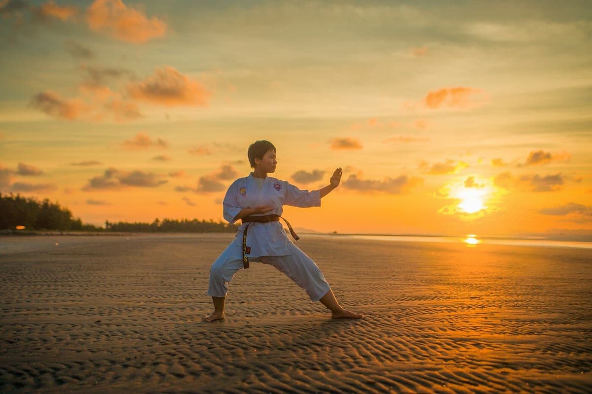 Praticante de karaté em posição de combate, na praia, ao pôr do sol